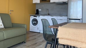 A compact living space with a sofa, a dining table with chairs, a washing machine, a microwave, and a refrigerator.