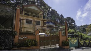 Un edificio de dos pisos con un balcón, una entrada con reja y un letrero que muestra una dirección web.