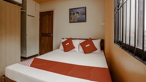 Habitación de hotel con cama, dos almohadas con la marca 'OYO', un cuadro de un paisaje urbano y una ventana con barrotes.