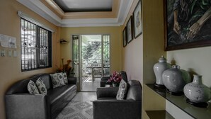 Una sala de estar con un sofá, un sillón y una mesa de centro de vidrio. Hay jarrones decorativos en una estantería y un cuadro en la pared.