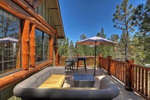 Une terrasse en bois agrémentée de meubles en osier, notamment d’un canapé et de deux tables, ainsi que d’un grand parasol.