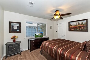 Un dormitorio con cama, ventilador de techo, cómoda, televisor, ventana con persianas y puerta.