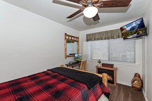 Une chambre à coucher comprenant un lit, un bureau, une chaise, une télévision, une cheminée et un ventilateur de plafond.