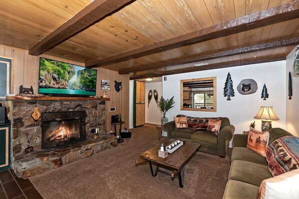 Una sala de estar acogedora con chimenea de piedra, un televisor montado en la pared y un ventanal grande.