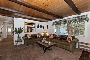 Una sala de estar acogedora con techo de madera, un sofá modular, una mesa de centro y un ventanal con vista a follaje.