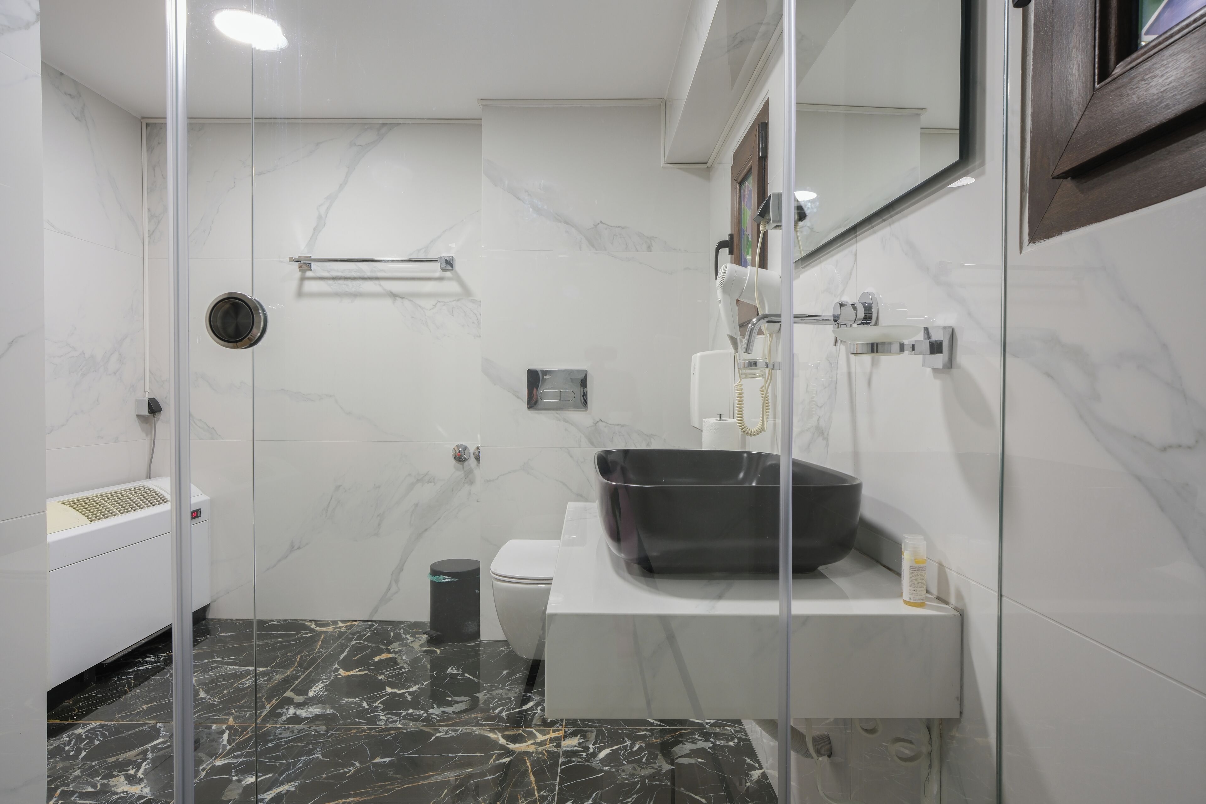 A modern bathroom with a glass shower enclosure, a black sink, and a marble-tiled floor.