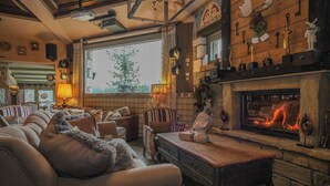 Una sala de estar acogedora con chimenea, sofás de cuero y un ventanal con vistas a árboles.