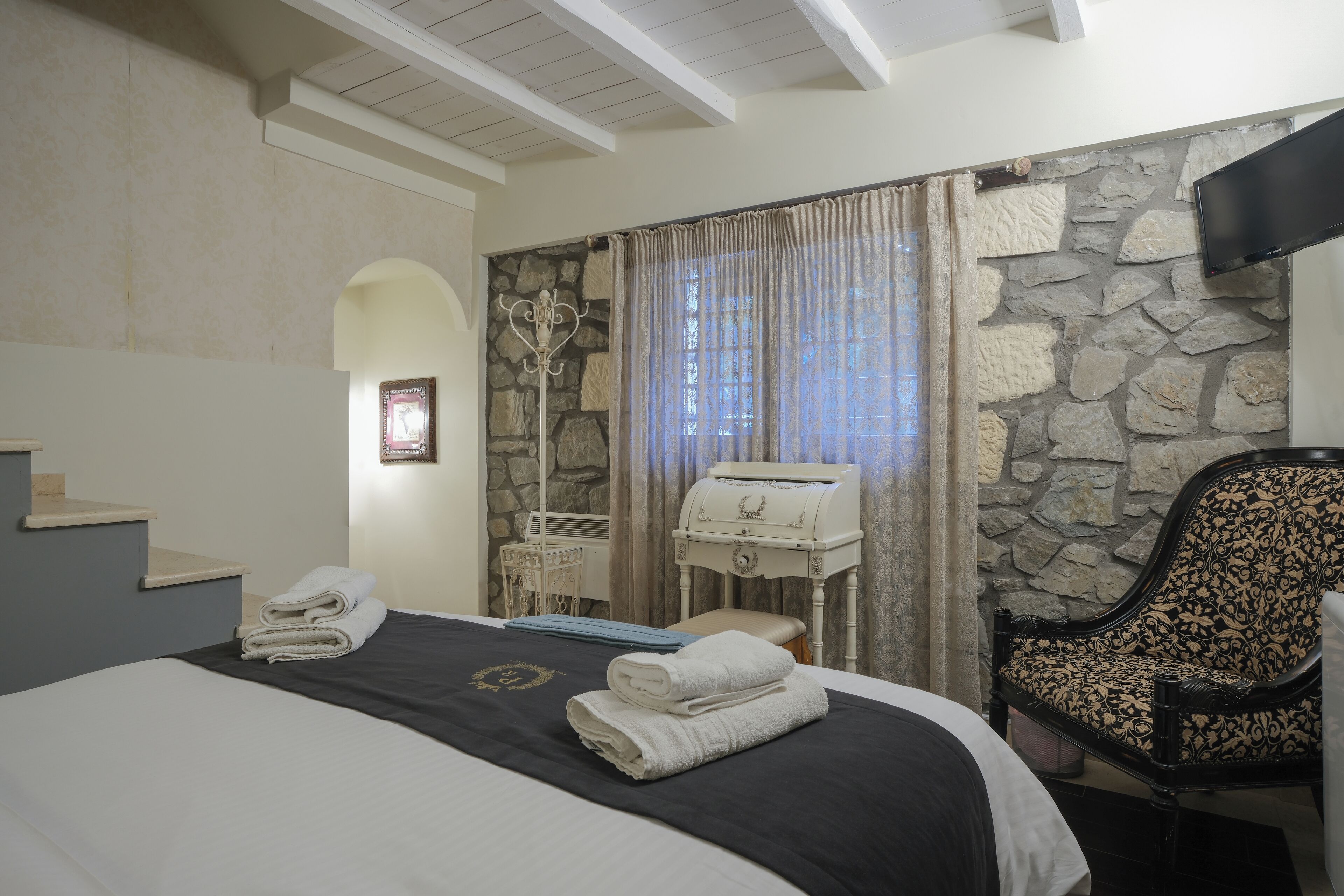 Habitación de hotel con cama, una silla, un escritorio y una pared de piedra.