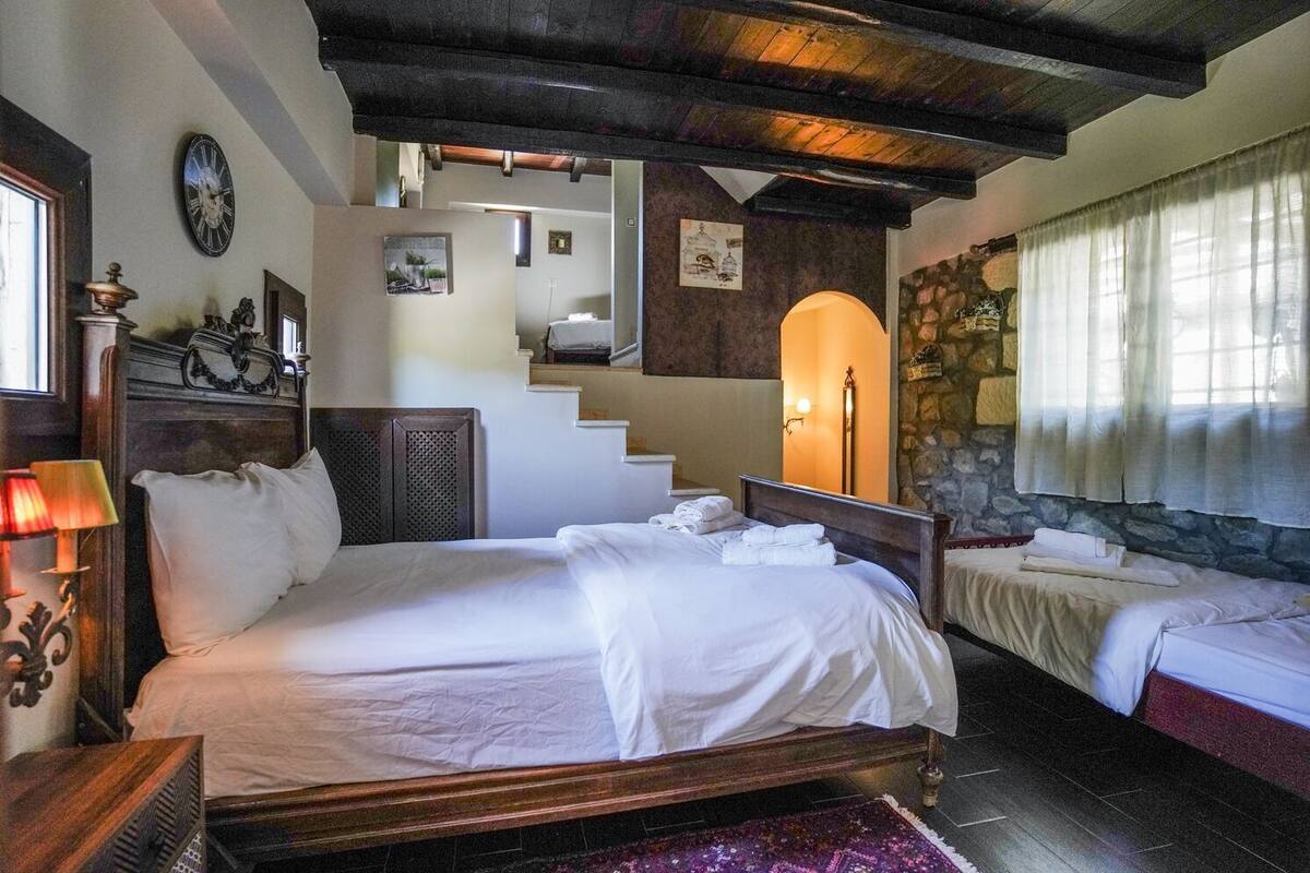 A hotel room with a large bed, a smaller bed, a staircase, and a stone wall.