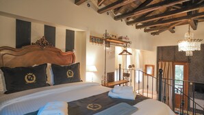 Habitación de hotel elegante con una cama grande, cabecera de madera, candelabro y balcón con vistas.