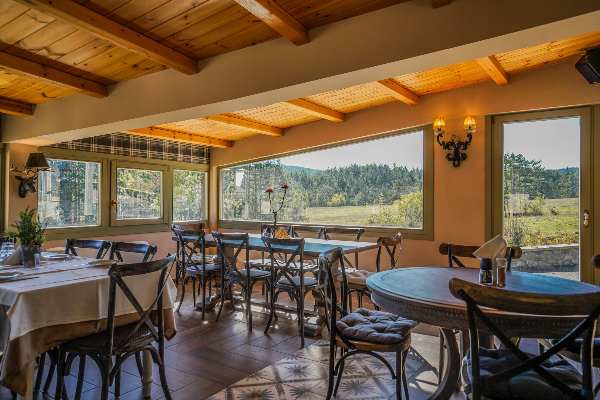 Un comedor con vigas de madera en el techo, grandes ventanas y vistas panorámicas, y sillas rústicas.