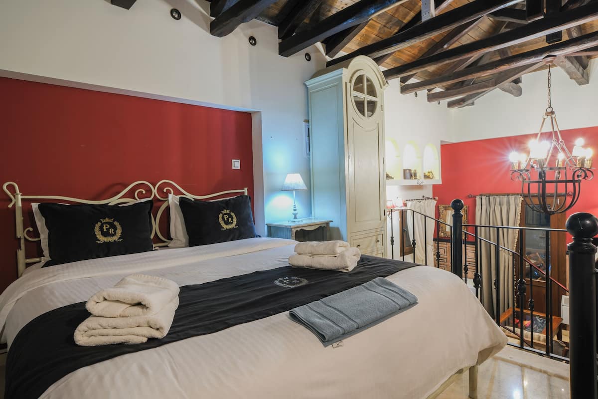 A neatly made bed with white and black bedding, a red wall, and a chandelier.