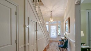 A hallway with a wooden floor, white doors, a chandelier, and a dining area with chairs and a table.
