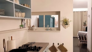 A modern kitchen with a gas stove, shelves with dishes, a mirror, and a dining area with a table and chairs. - House with land LES MATHES/LA PALMYRE (Les Mathes)