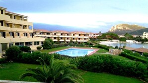 A hotel with multiple balconies, a swimming pool, and a view of a mountain and sea. - Terza Spiaggia la Filasca (Golfo Aranci)