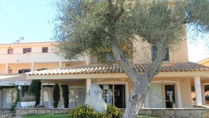 A building with a tiled roof, stone walls, and a tree in the foreground. - Terza Spiaggia la Filasca (Golfo Aranci)