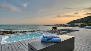 A wooden deck with a hot tub and a barbecue grill, overlooking the ocean. - Marlin Manor (Struisbaai)
