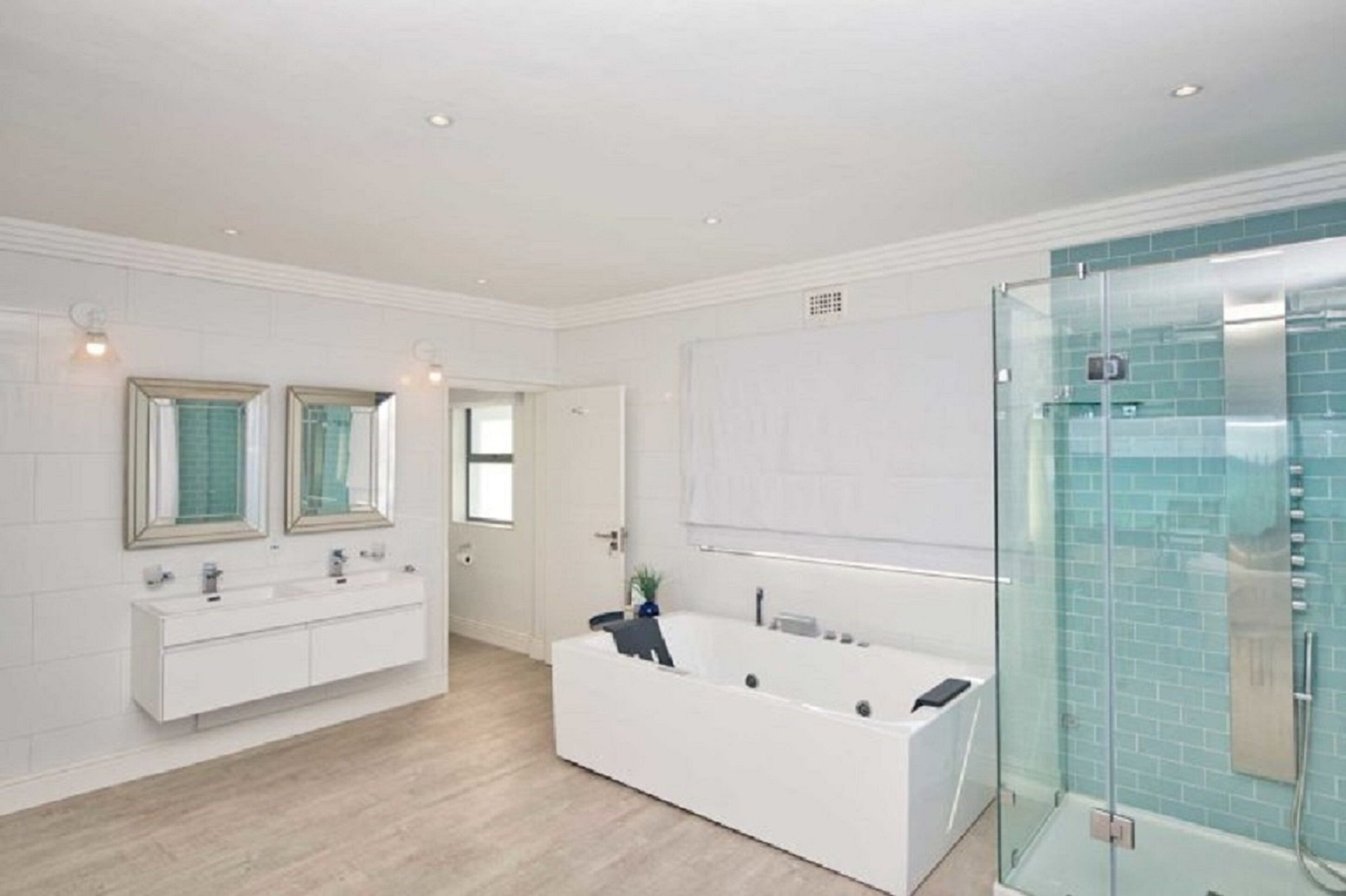 A modern bathroom with a large white bathtub, a glass-enclosed shower, and two vanity sinks with mirrors.