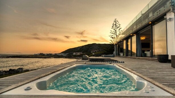 A hot tub on a wooden deck with a view of the sea and a mountain in the background. - Marlin Manor (Struisbaai)