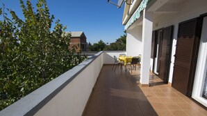 Een balkon met betegelde vloer, een kleintje tafeltje en stoelen, en een gebouw op de achtergrond.