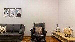 Una sala de estar con un sofá y un sillón de cuero negro, una mesita de madera con un globo terráqueo y un florero a rayas, y tres obras de arte abstracto en la pared.