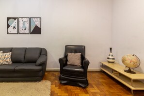 A living room with a black leather sofa, a black leather chair, a small wooden side table with a globe and a striped vase, and three abstract wall art pieces. - 2 Minutes From Copacabana Beach A306 (Rio de Janeiro)