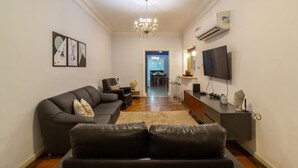 Una sala de estar moderna con un sofá de cuero negro, una araña, un televisor de pantalla plana y una decoración minimalista.