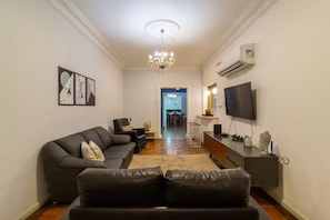 A modern living room with a black leather sofa, a chandelier, a flat-screen TV, and a minimalist decor. - 2 Minutes From Copacabana Beach A306 (Rio de Janeiro)