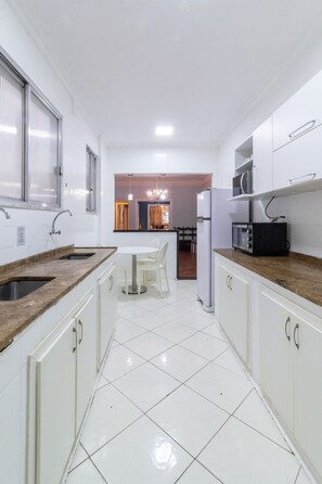 Una cocina con gabinetes blancos, un lavamanos doble, un microondas y un refrigerador.