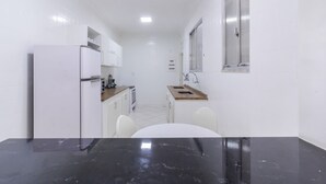 Una cucina compatta con mobili bianchi, un frigorifero, un lavandino e una finestra.