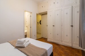 Un dormitorio con cama, armario y baño visible a través de una puerta abierta.