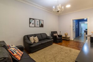 A living room with a black leather sofa, a black armchair, and a beige rug. There are three framed artworks on the wall.
