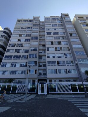 Un edificio residencial de varios pisos con fachada uniforme, ventanas grandes y acceso por portón.