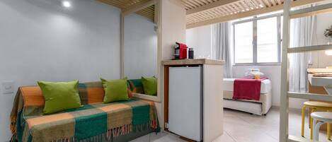 Una habitación moderna con sofá, un refrigerador pequeño, una ventana con cortinas y un escritorio con silla.