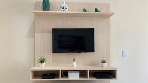 A modern living room with a mounted TV, wooden shelves, and two small potted plants.