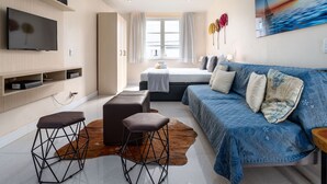 A modern bedroom with a bed, a TV, a sofa, and a large window.