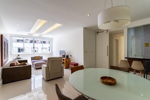 Uma sala de estar moderna com uma mesa de jantar de vidro, sofás e uma grande janela.