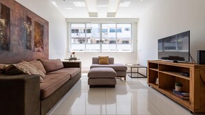 A modern living room with a large window, a sofa, a coffee table, and a TV on a wooden stand.