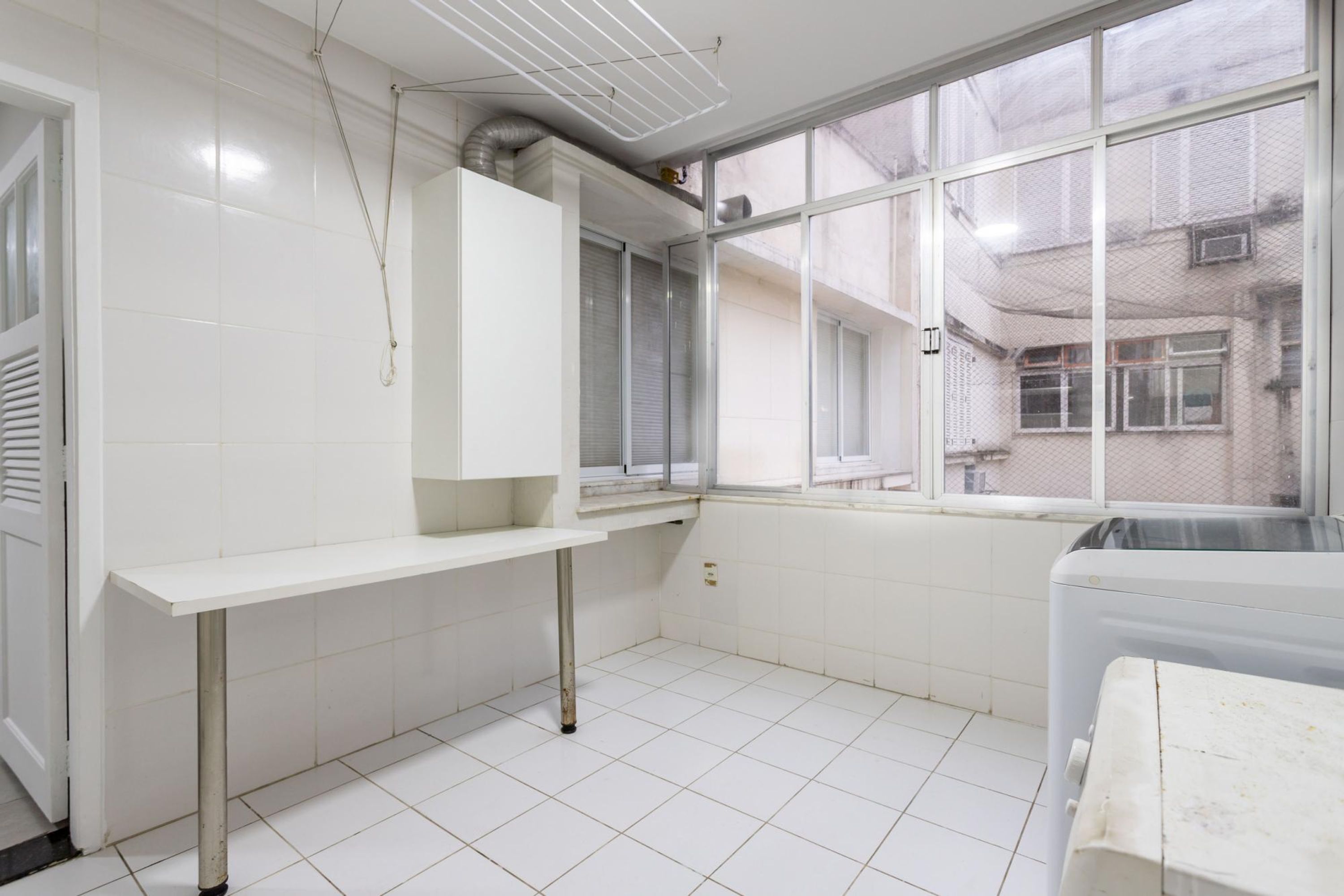 A kitchen with white tiles, a window, and a drying rack.