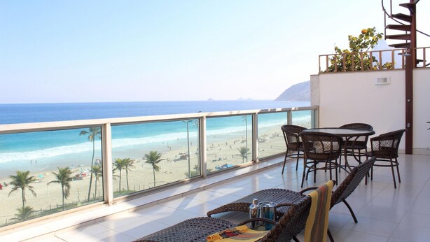 A balcony with a view of the beach and ocean. There are wicker chairs and a table with a bottle and a glass. - Penthouse With sea View on the Beachfront Vsc1 (Rio de Janeiro)