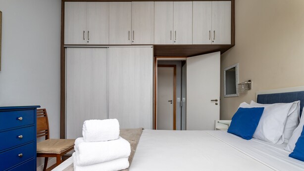 A bedroom with a bed, a wardrobe, a chair, and a stack of towels. - Copacabana Ideal for Couples Rpp913 (Rio de Janeiro)