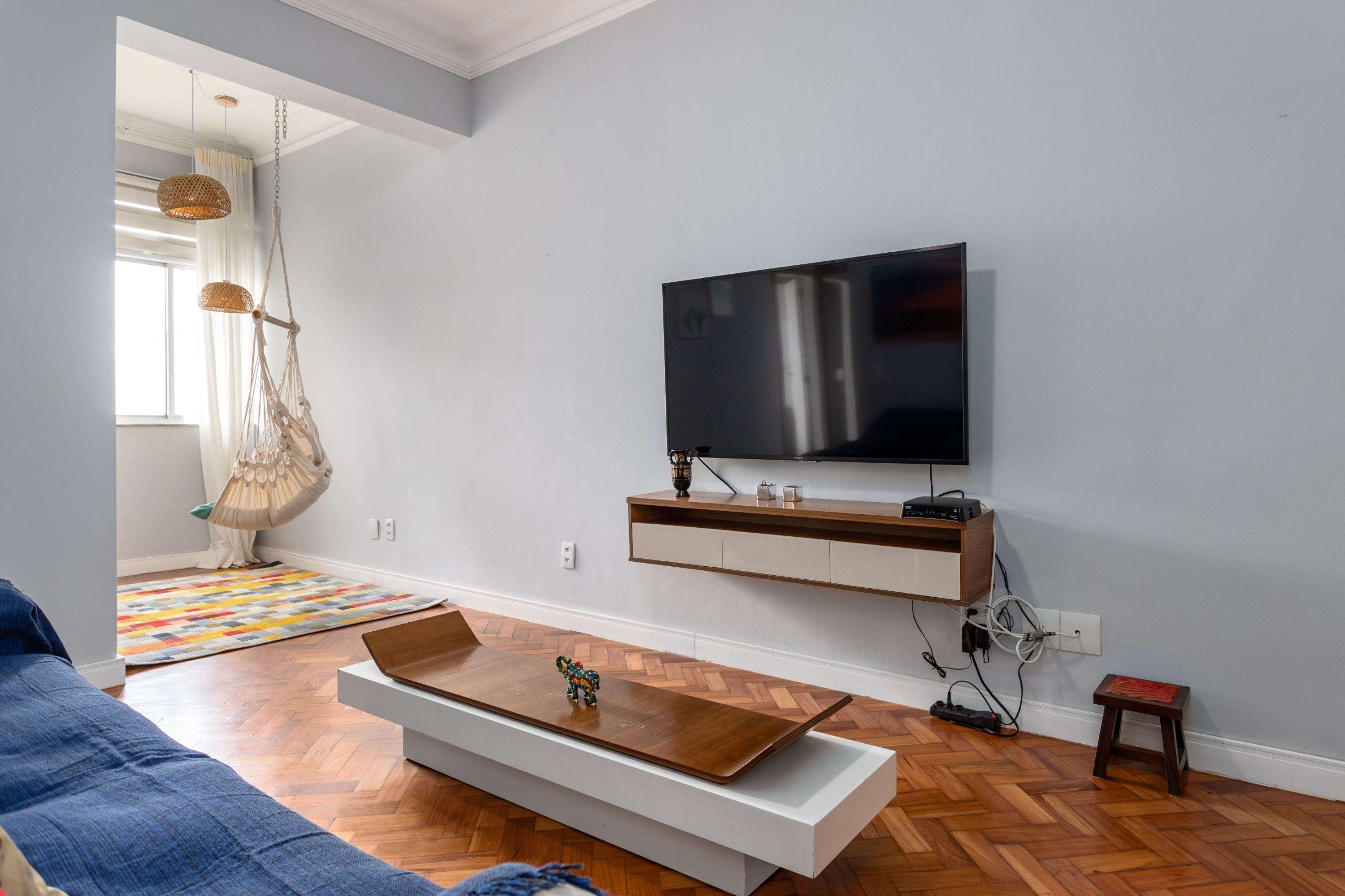 A modern living room with a flat-screen TV mounted on the wall, a wooden coffee table, a blue sofa, and a herringbone-patterned floor.