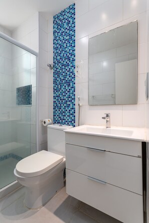 A bathroom with a white toilet, a sink with a mirror, and a shower area.