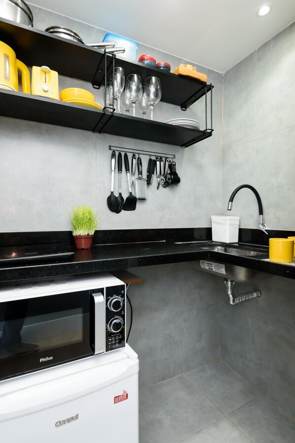 A modern kitchen with a black countertop, a white dishwasher, and a black stove. There are shelves above the counter holding various kitchen items, and a potted plant on the counter.