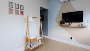 Una habitación moderna con una silla mecedora de madera, un televisor montado en la pared y un estante con una planta.