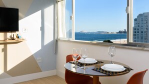 Un comedor con una mesa preparada para dos personas, dos copas de vino y vistas al océano y edificios.