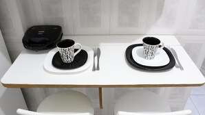 Une petite table à manger avec deux tasses aux motifs noir et blanc, une assiette noire et blanche, ainsi qu’une fourchette et un couteau noirs et blancs.