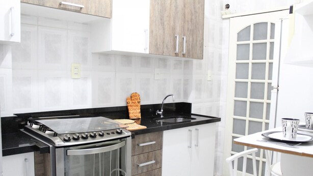 Une cuisine moderne dotée d’une cuisinière en acier inoxydable, d’un plan de travail noir, de meubles blancs et d’un petit coin repas avec une chaise et une table blanches.