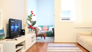 Un salon équipé d’un téléviseur à écran plat, d’un meuble de rangement blanc, d’un canapé, d’un tapis à motifs et d’une plante en pot.