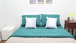 Un lit avec une couvre-lit de couleur turquoise et deux oreillers, une table de chevet avec une lampe, et trois tableaux encadrés accrochés au mur.